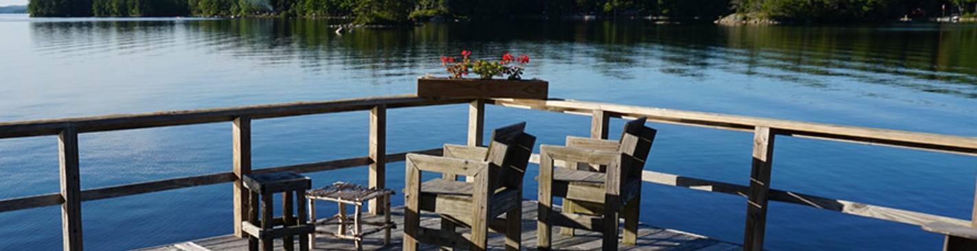 A wooden deck at Leen's Lodge in Maine, overlooking lake, with two chairs and a flowerbox on the railing.